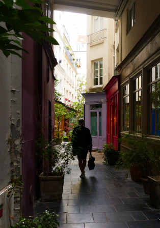 Une silhouette de dos, dans l'ombre, emprunte un passage parisien aux façades colorées.