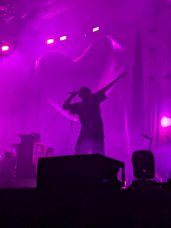 Grian Chatten, en contre jour devant le coeur symbolique de l'album Romance, bras ouverts, sur scène en novembre dernier.