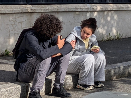 Un garçon et une fille, adolescents, se parlent avec animation, assis sur un trottoir à l'arrêt du bus près de la gare.